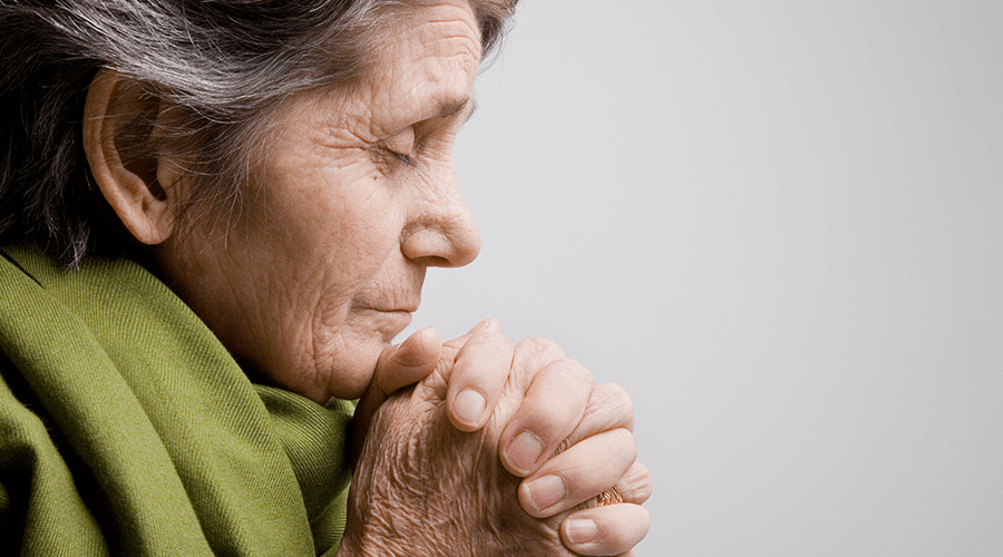 Older woman praying with closed eyes and folded hands