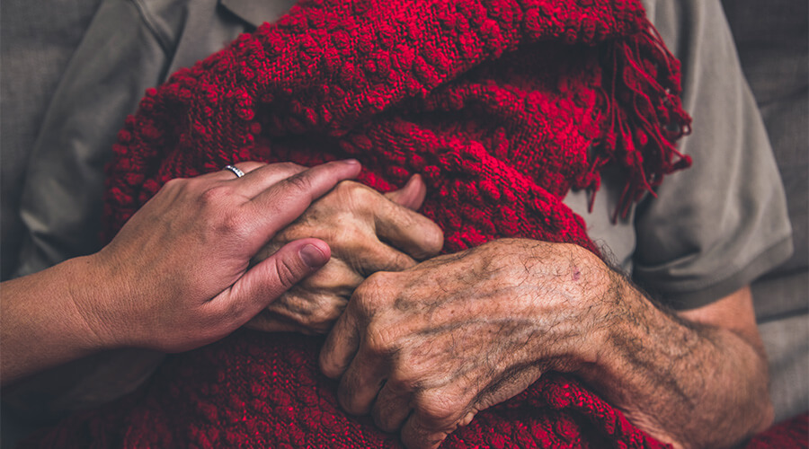 Elderly gentleman in hospice care clutching a red blanket.