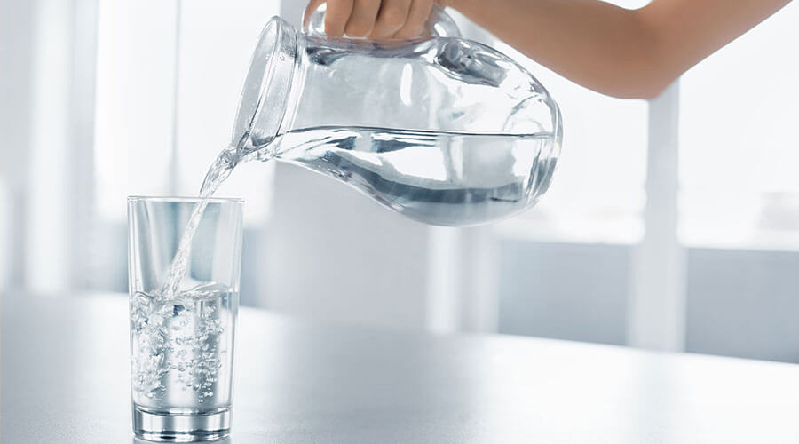 Person pouring water into a glass from a pitcher.