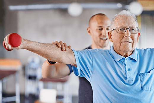 Male physical therapist assisting a senior male lift weights
