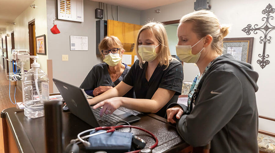 Registered Nurse, Anna Struck, talking with colleagues at a computer at Good Samaritan Society - Scotland in Scotland, South Dakota.