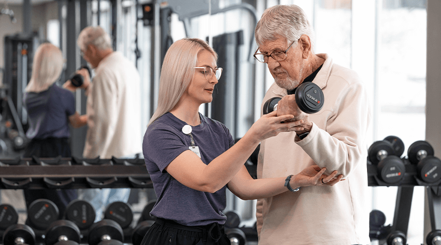 A female physical therapist assisting a male patient with lifting exercise.