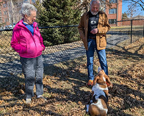 Dog sitting in front of two people in the park